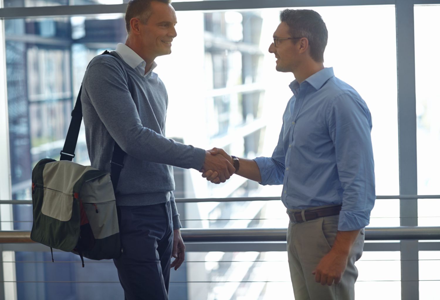 two young men shaking hands in sky office building representing Partnership for the Employee Staffing Industry.