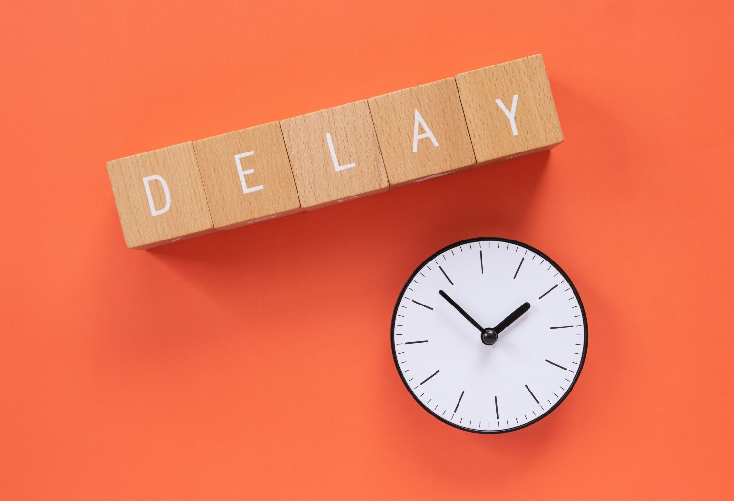 A clock and the words Delay on word blocks sitting on an orange background. Image representing payment delays in employee staffing.